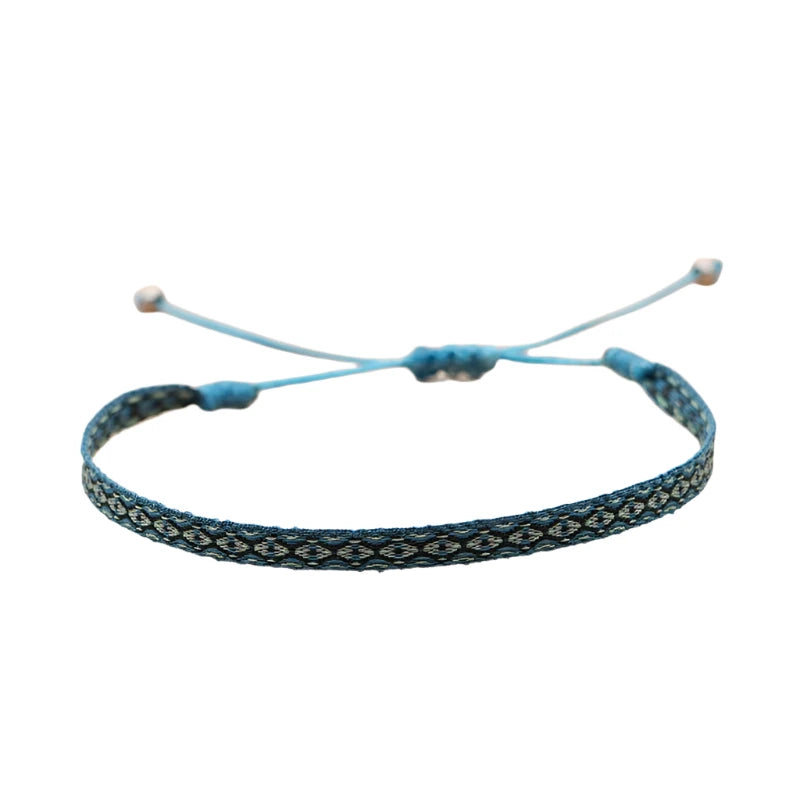 Woven bracelet with a blue and turquoise diamond pattern, worn on wrist alongside other bracelets.