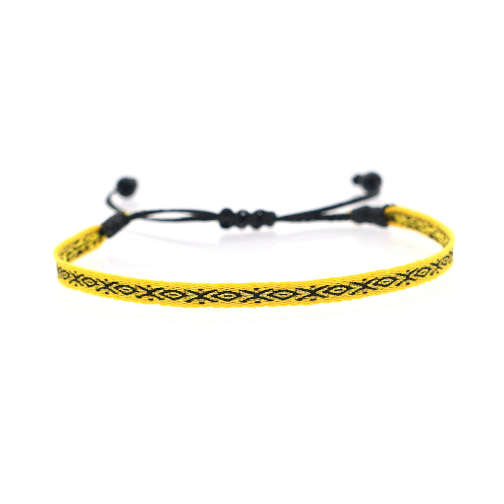 Yellow woven bracelet with black geometric patterns and adjustable black cord.