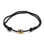 Black braided bracelet with a gold and blue evil eye charm on a white background
