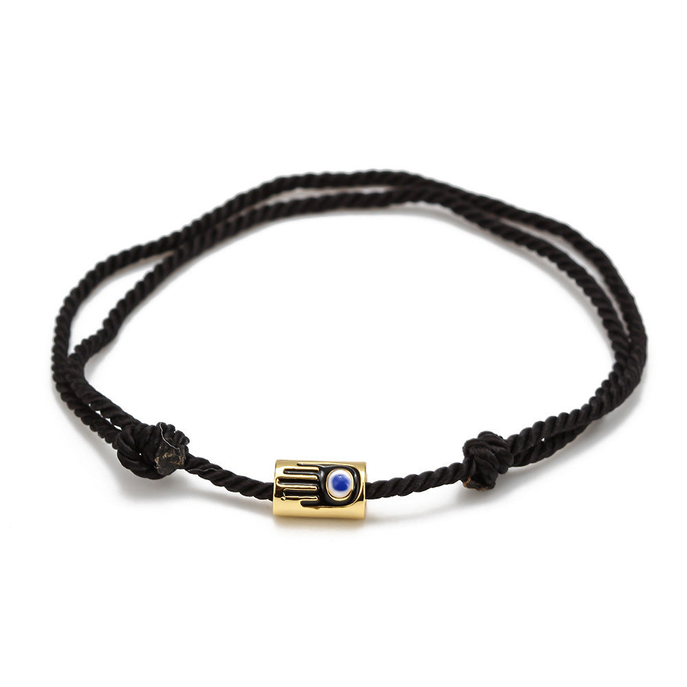 Black braided bracelet with a gold and blue evil eye charm on a white background