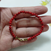 Red beaded bracelet with gold accents on a hand against a white background