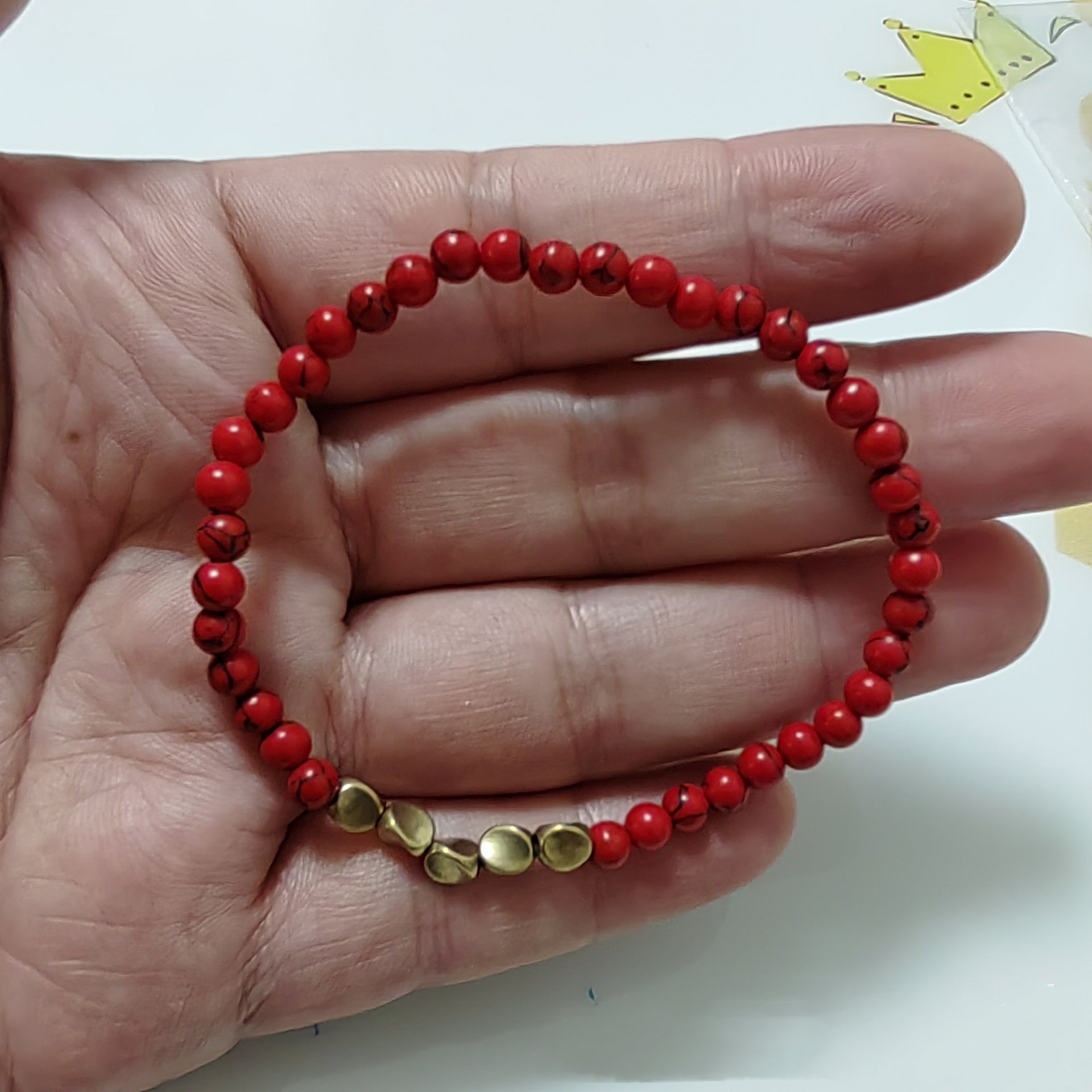 Red beaded bracelet with gold accents on a hand against a white background