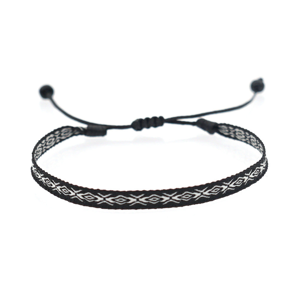 Black woven bracelet with white geometric pattern and adjustable black cord.