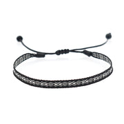 Black woven bracelet with white geometric pattern and adjustable black cord.