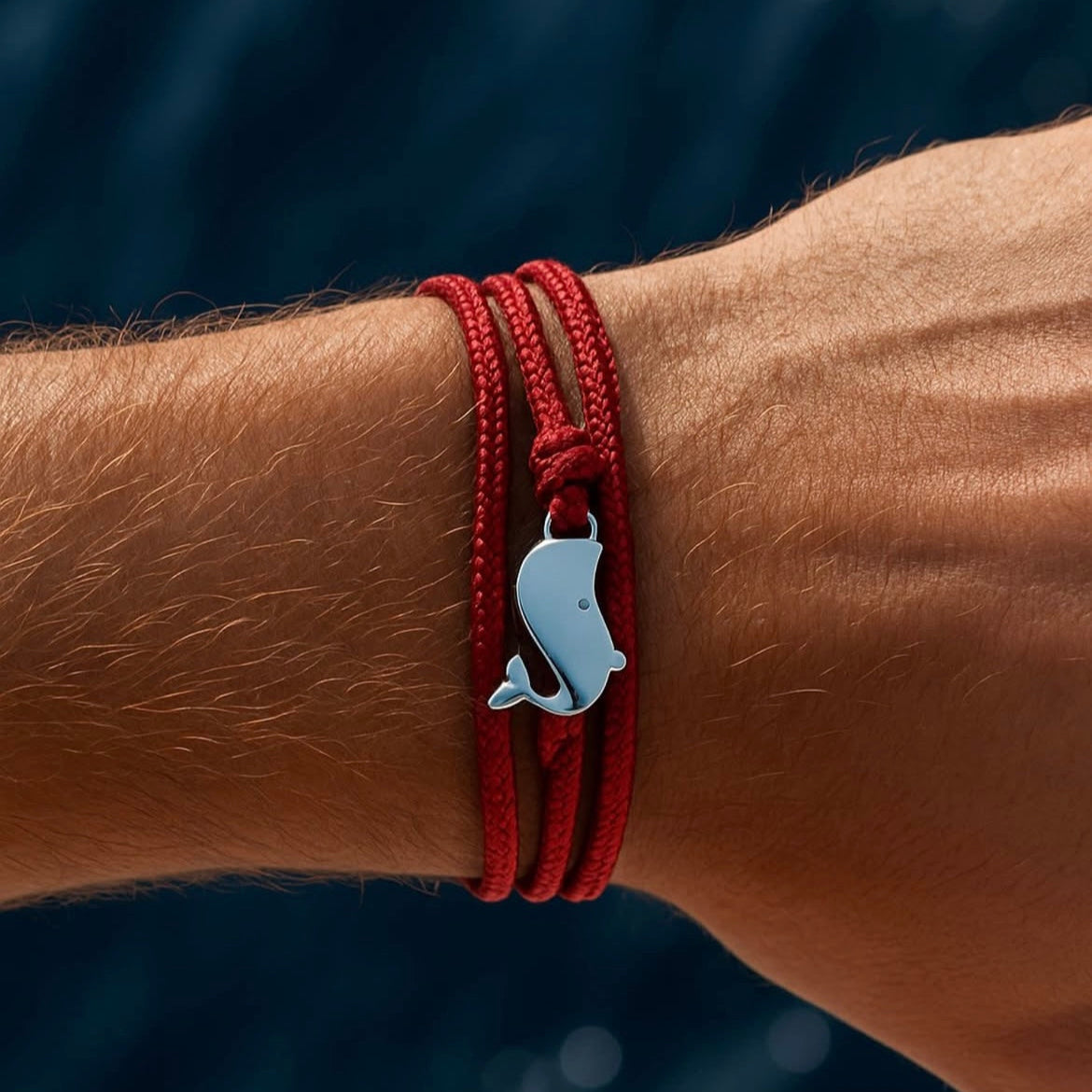 Red bracelet with a silver dolphin charm on a wrist against a blurred natural background