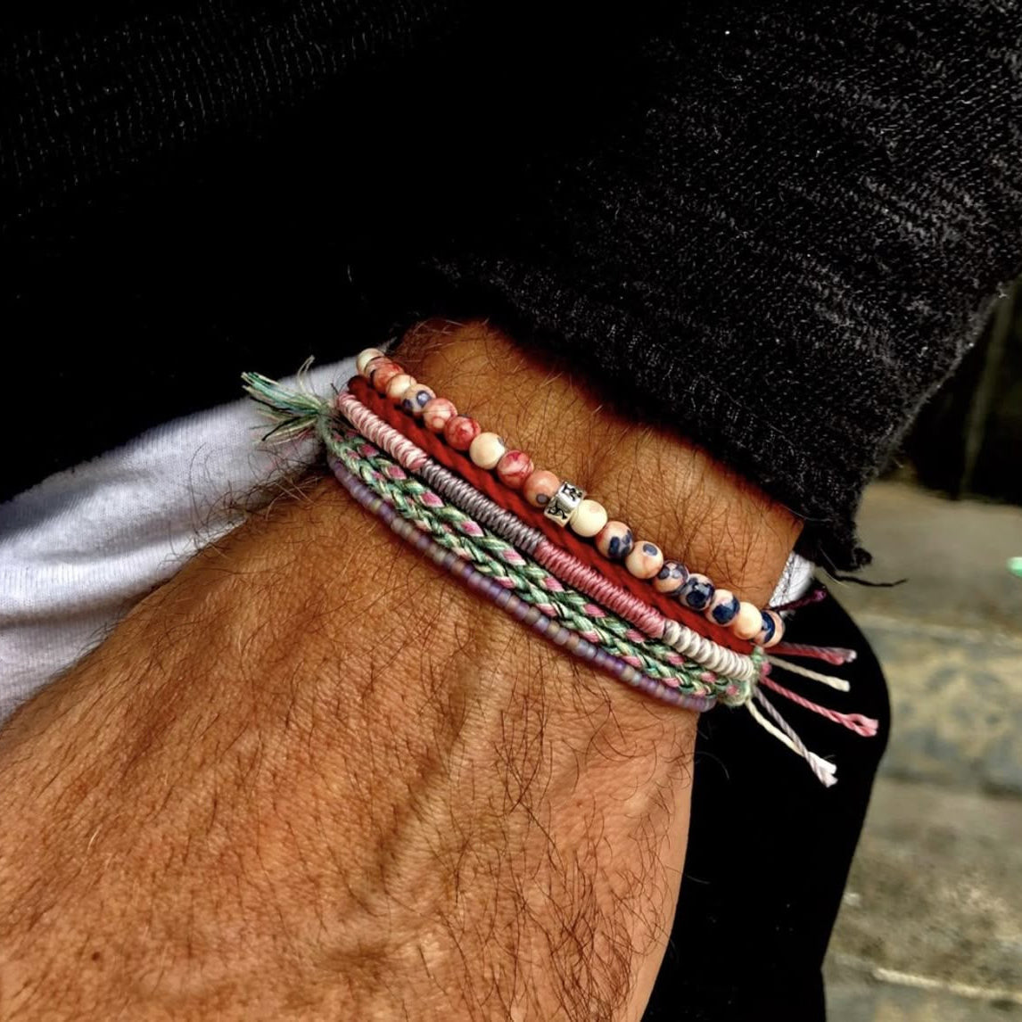Close-up of a person's wrist with multiple colorful bracelets on a blurred background