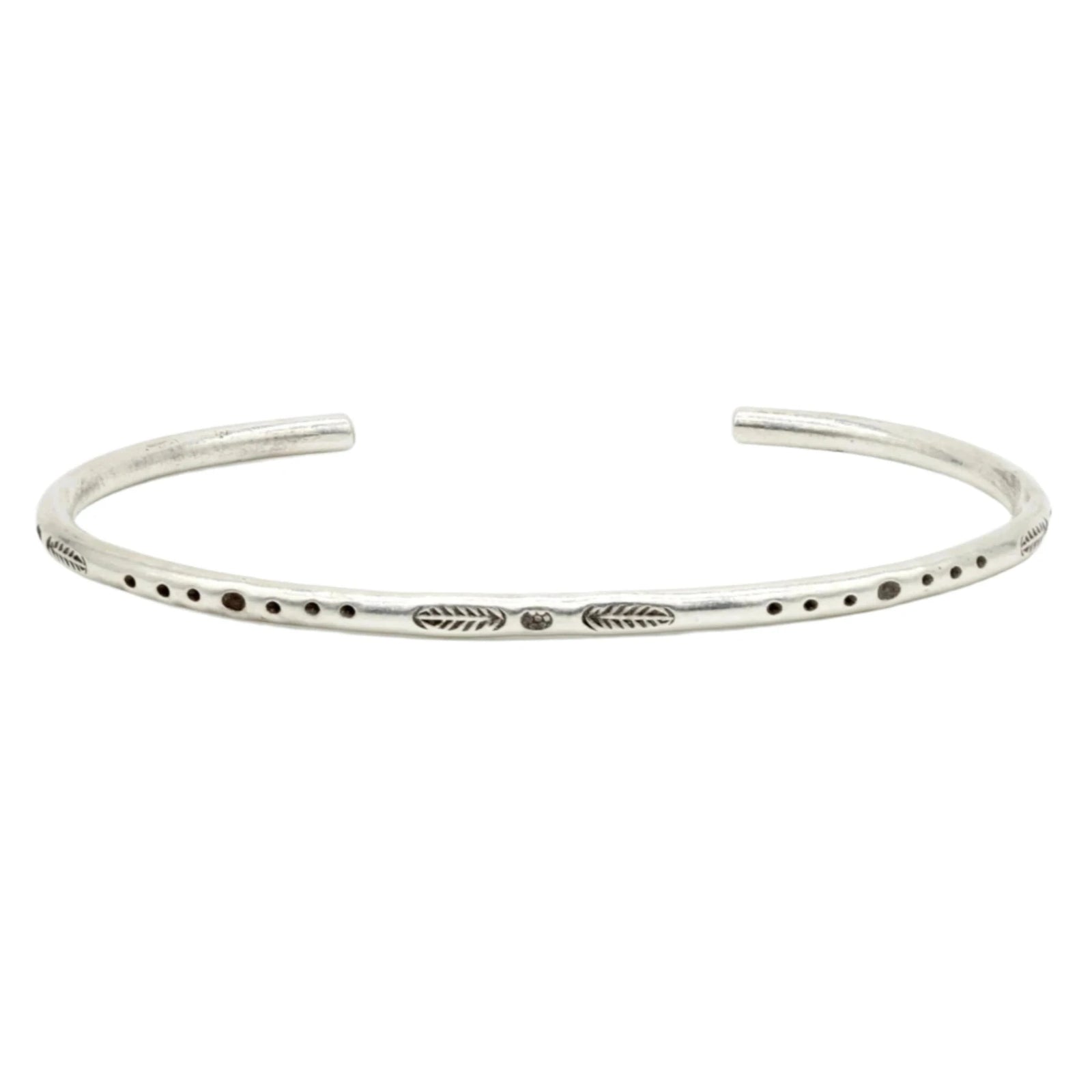 Silver-toned cuff bracelet with etched dot and line engravings, worn on wrist with other bracelets.