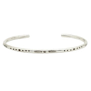 Silver-toned cuff bracelet with etched dot and line engravings, worn on wrist with other bracelets.
