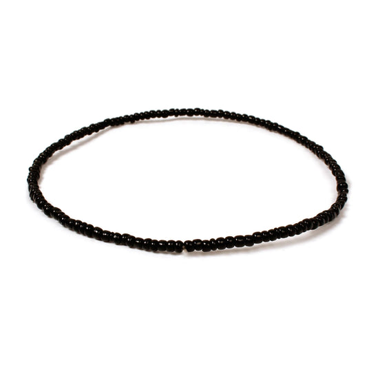 Handmade black beaded bracelet with small glossy glass beads arranged in a minimalist circular design on a white background