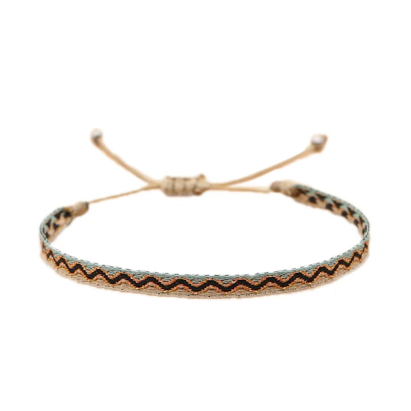 Flat woven bracelet featuring zig-zag patterns in black, turquoise, and tan, resembling traditional coastal motifs.