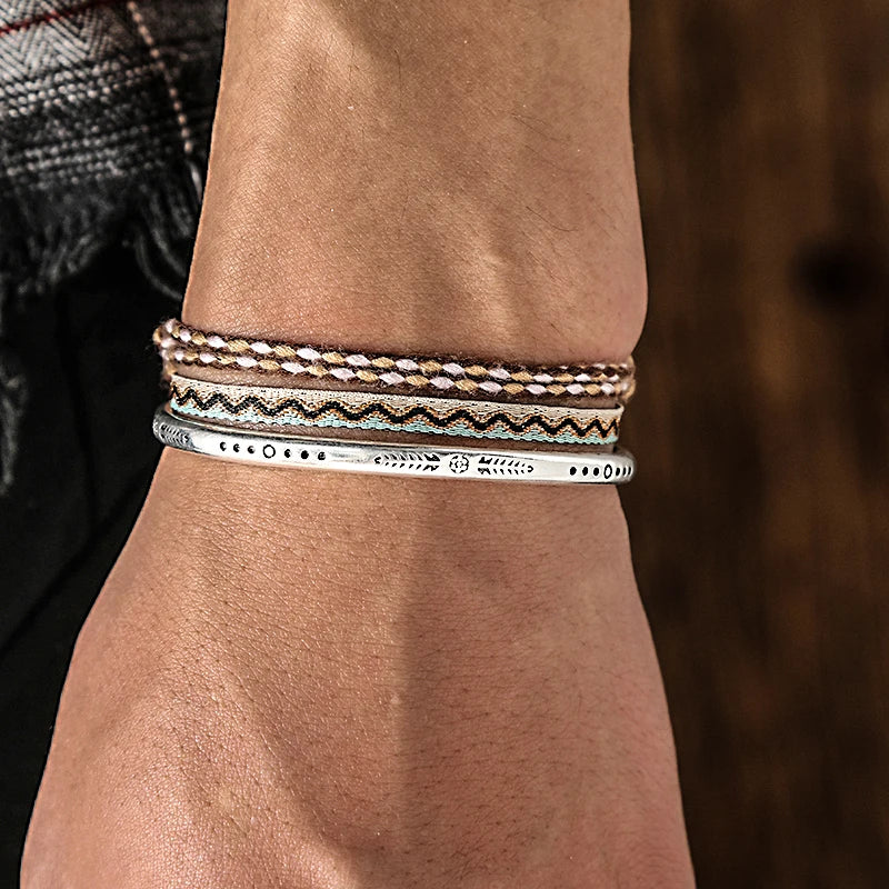 Stacked Aegean Earth bundle worn on wrist, combining neutral braids, zig-zag weaves, and a silver cuff for a stylish layered look.