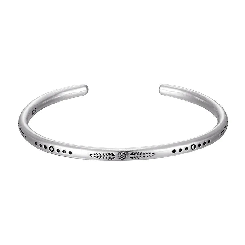 Silver-toned cuff bracelet with etched dot and line engravings, worn on wrist with other bracelets.