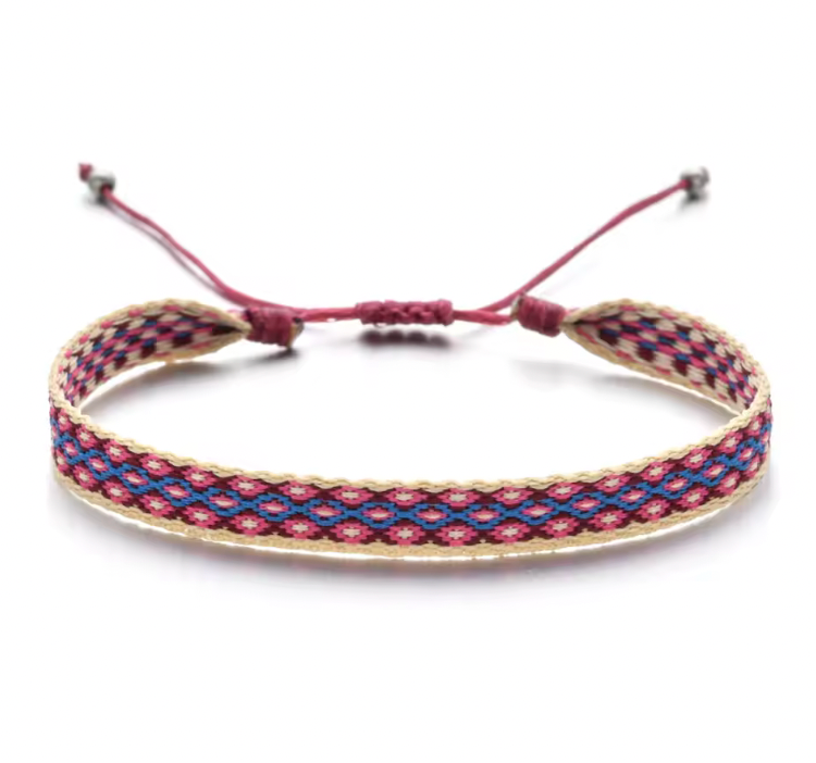 Earth-tone handmade woven bracelet in terracotta and green hues, displayed on a neutral round surface with an adjustable brown cord.