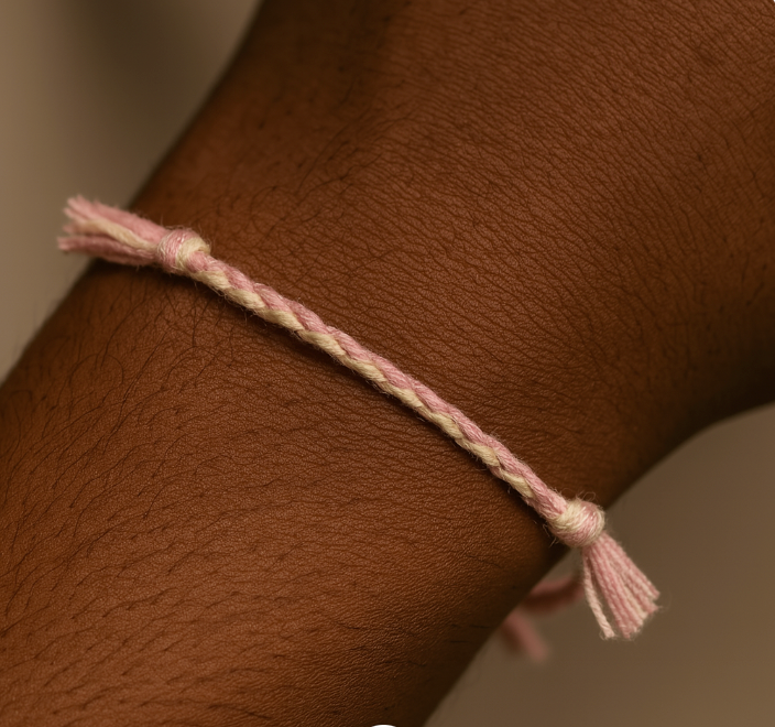 Close-up of a wrist wearing a pink woven bracelet against a neutral background