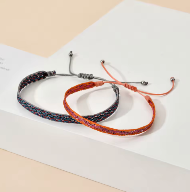 Two braided bracelets, one black and one orange, on a light beige background.