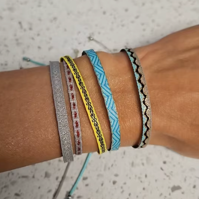 Wrist with multiple colorful bracelets on a speckled surface
