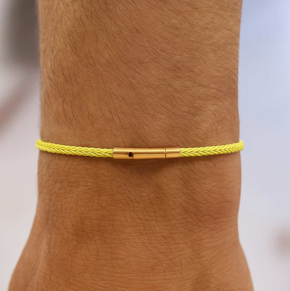 Yellow braided bracelet with gold clasp on a wrist against a neutral background
