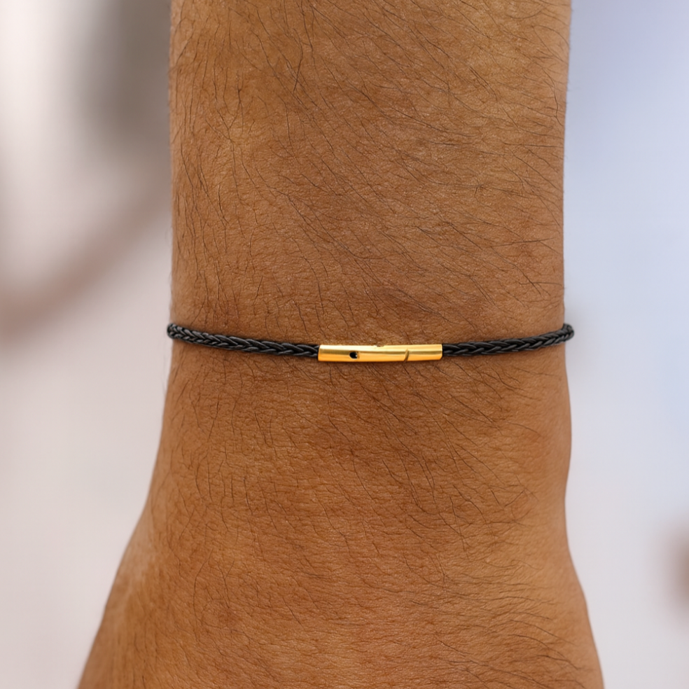 Black bracelet with a gold clasp on a wrist against a neutral background