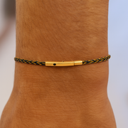 Gold and black braided anklet on a person's ankle with a blurred background
