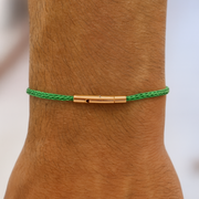 Green braided bracelet with gold clasp on a wrist against a neutral background