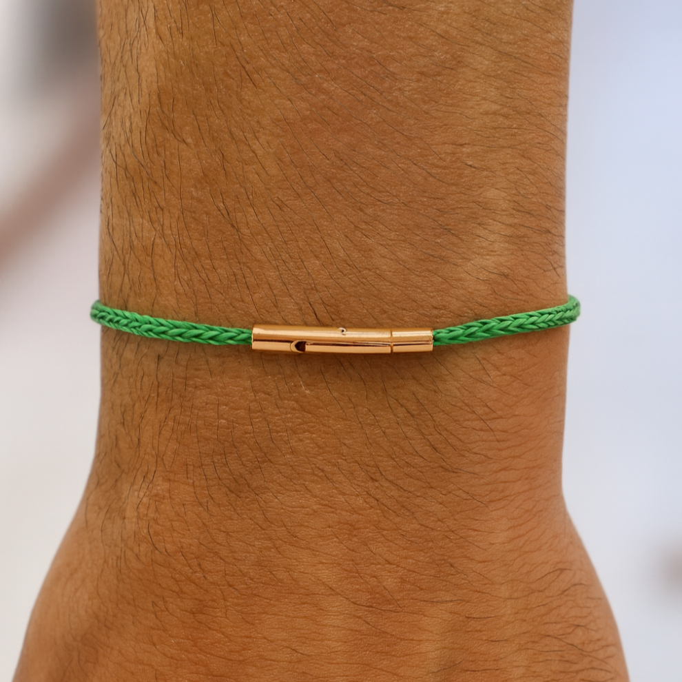 Green braided bracelet with gold clasp on a wrist against a neutral background