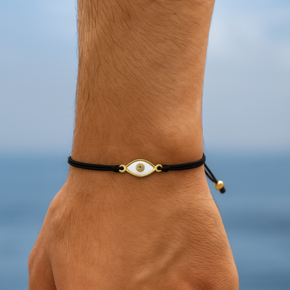 Hand wearing a black bracelet with a gold clasp against a blurred ocean background
