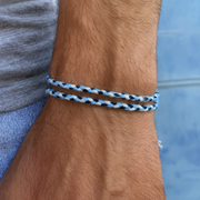 Close-up of a wrist wearing a braided blue, black, and white bracelet with a blurred background.
