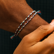 Close-up of a wrist wearing a braided bracelet with red, white, and blue strings.