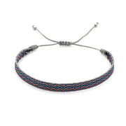 Handwoven bracelet with blue, red, and grey pattern on adjustable cord, inspired by Mediterranean design.