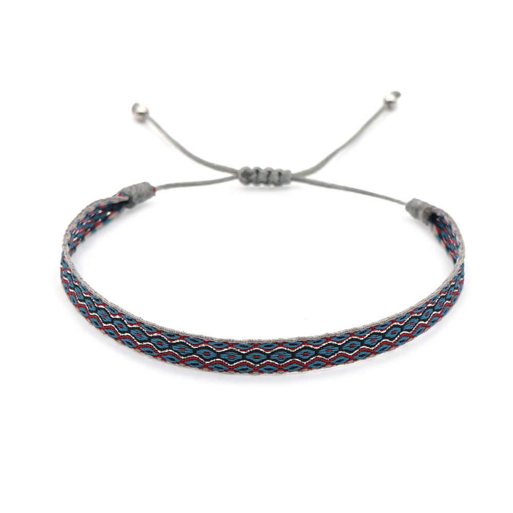 Handwoven bracelet with blue, red, and grey pattern on adjustable cord, inspired by Mediterranean design.