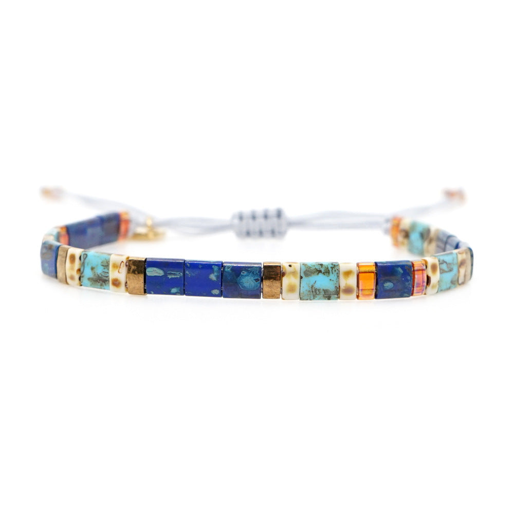 Handmade “Santorini Mosaic” beaded bracelet by Rue & Strand, featuring square beads in lapis blue, turquoise, amber, and ivory with a light grey adjustable cord.