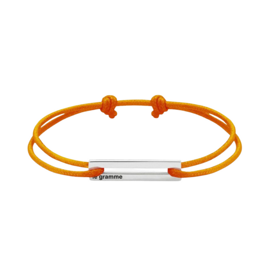 Orange cord bracelet with minimalist silver metal bar, laid flat on a white background.